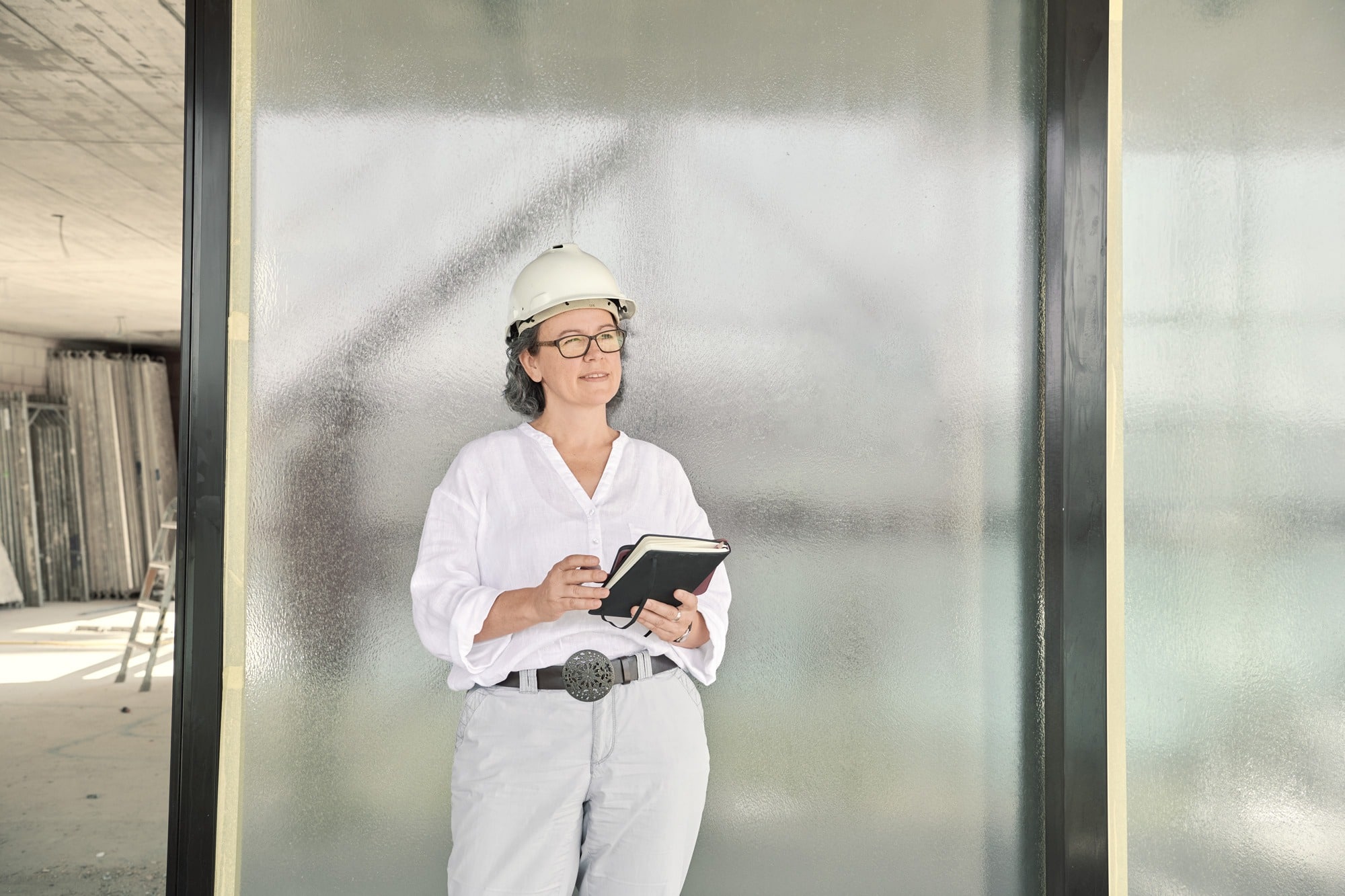 Architektin mit einer weissen Bluse und Baustellenhelm hält ein schwarzes Notizbuch in den Händen