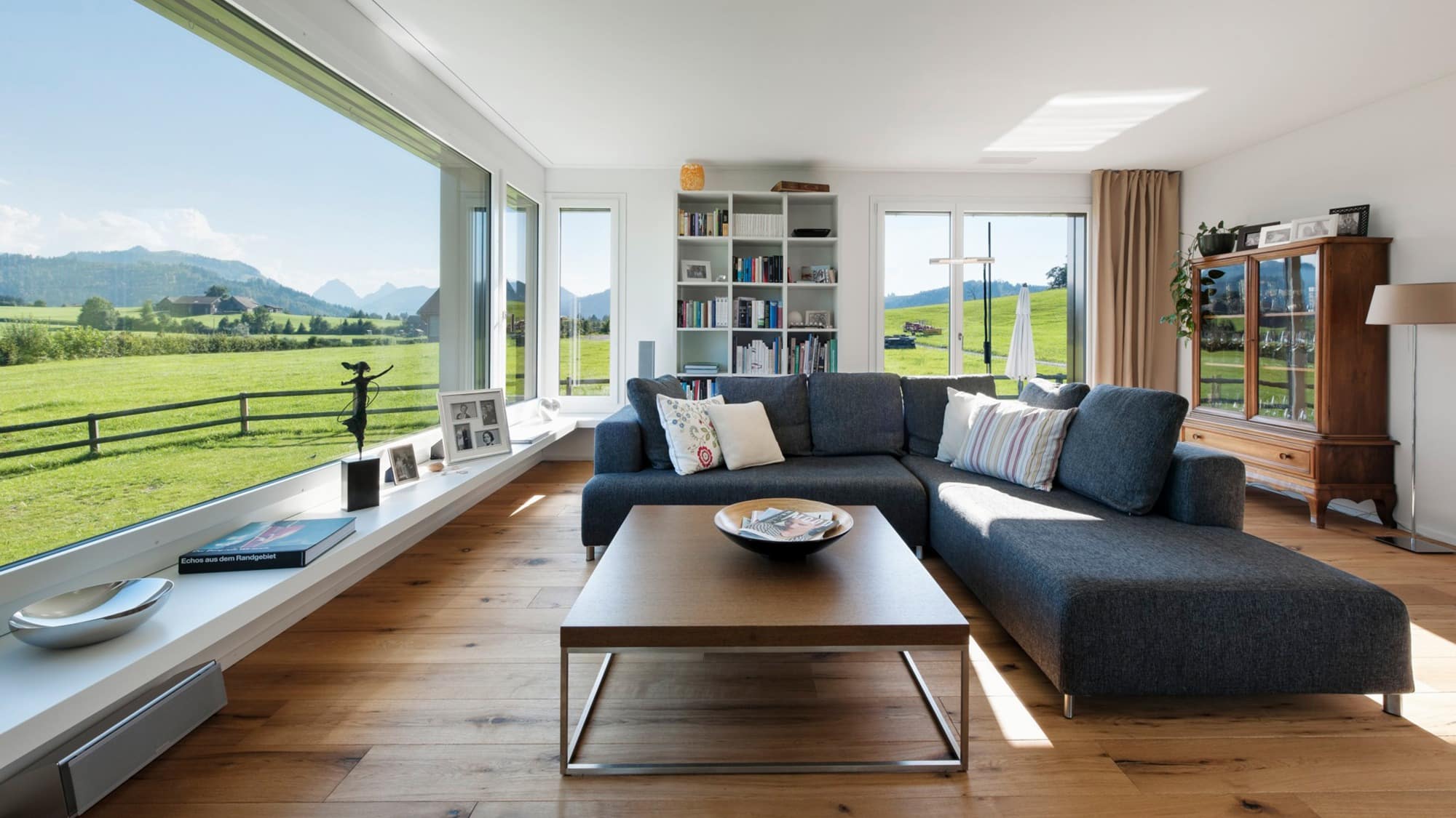 Wohnzimmer mit dunkelgrauem Sofa, braunem Tisch und grossem Sitzfenster