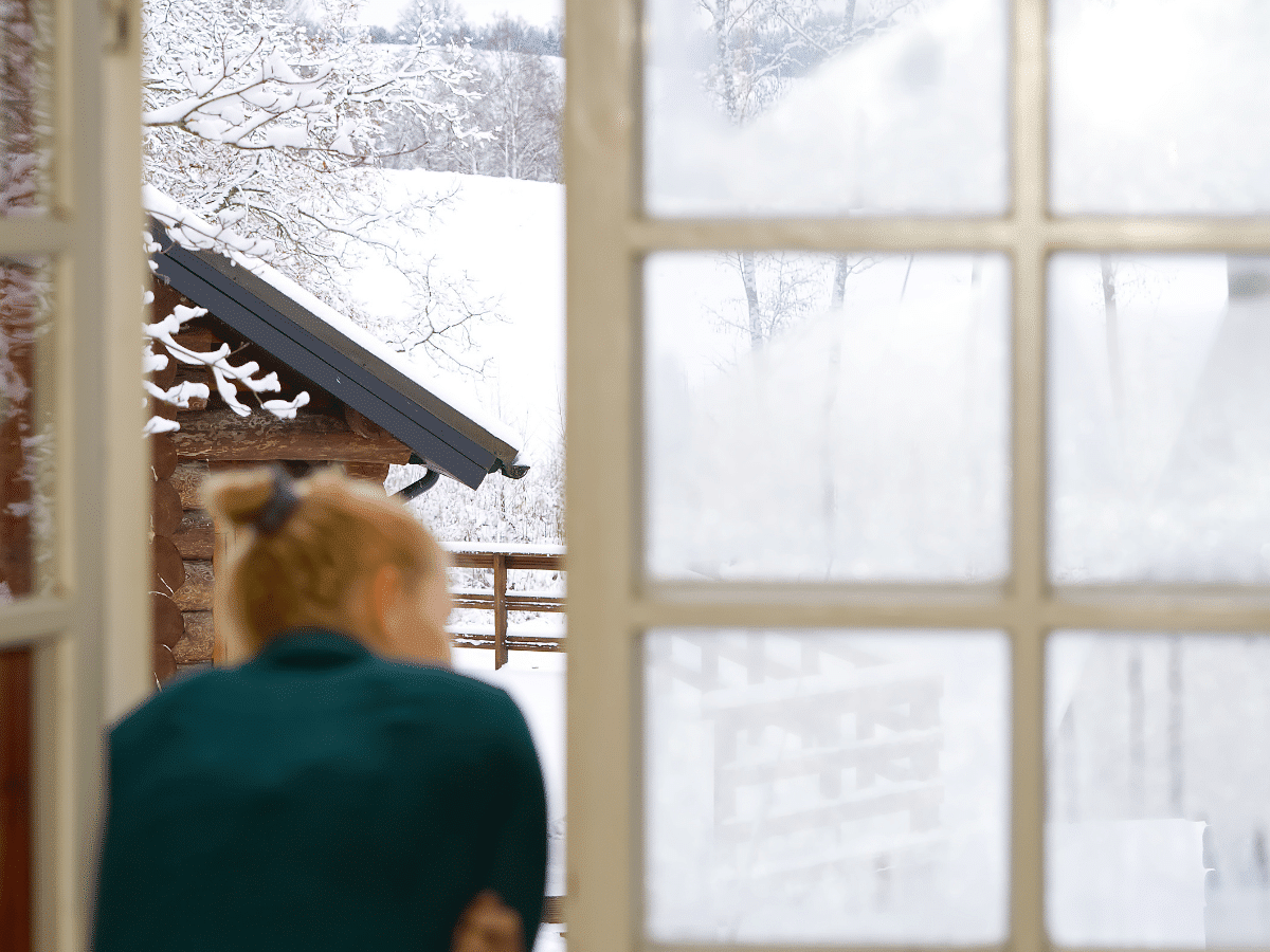 Lüften im Winter, Frau schaut aus dem Fenster mit Sprossen