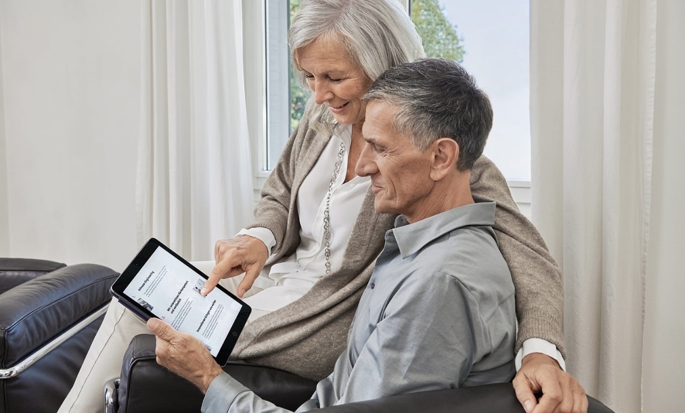 Älteres Ehepaar sitzt zusammen und schaut gemeinsam auf ein Tablet