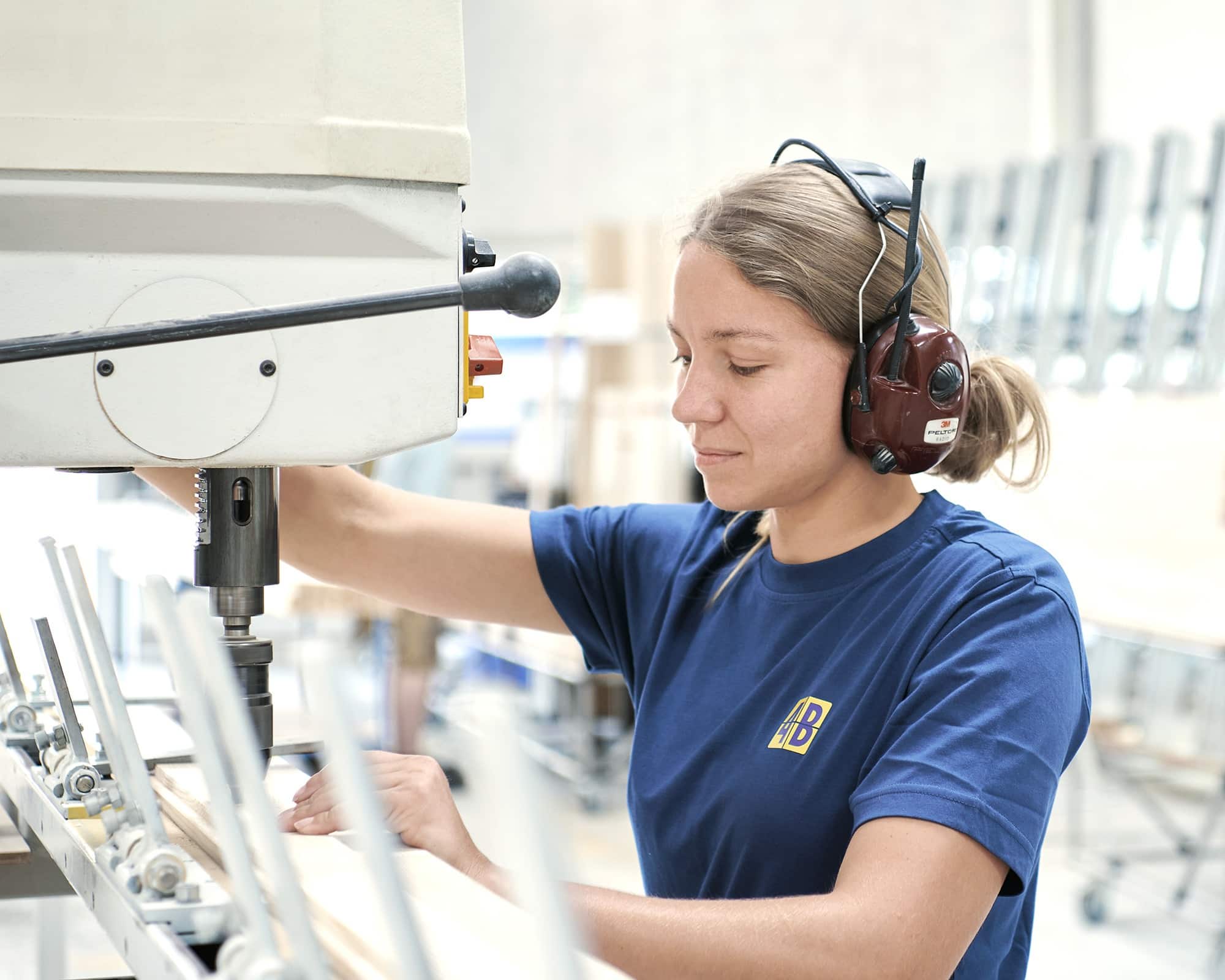 Auszubildende Schreinerpraktikerin bohrt mit Bohrmaschine ein Loch in ein Stück Holz