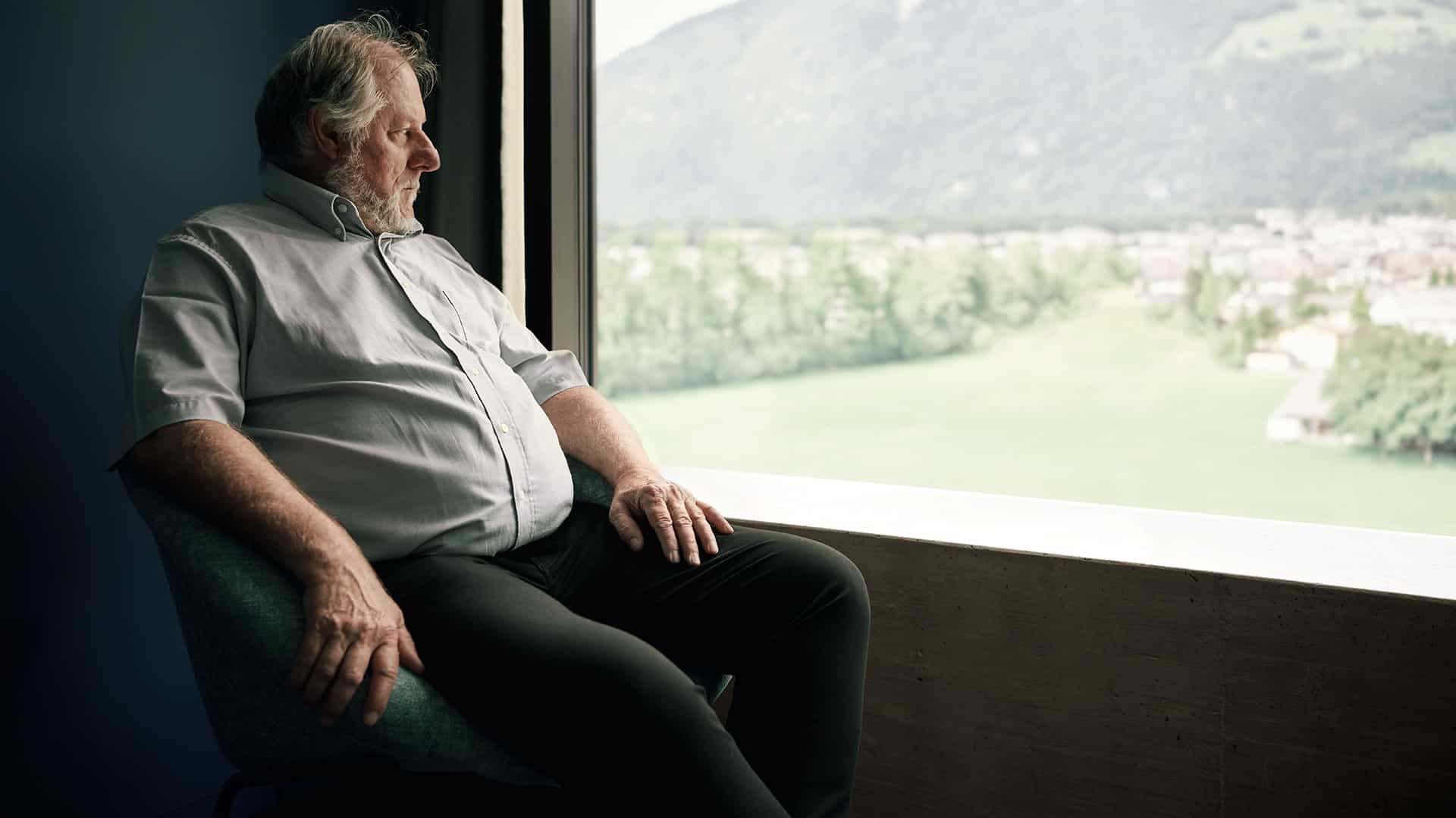 Mann sitzt auf einem Stuhl und schaut aus dem Fenster