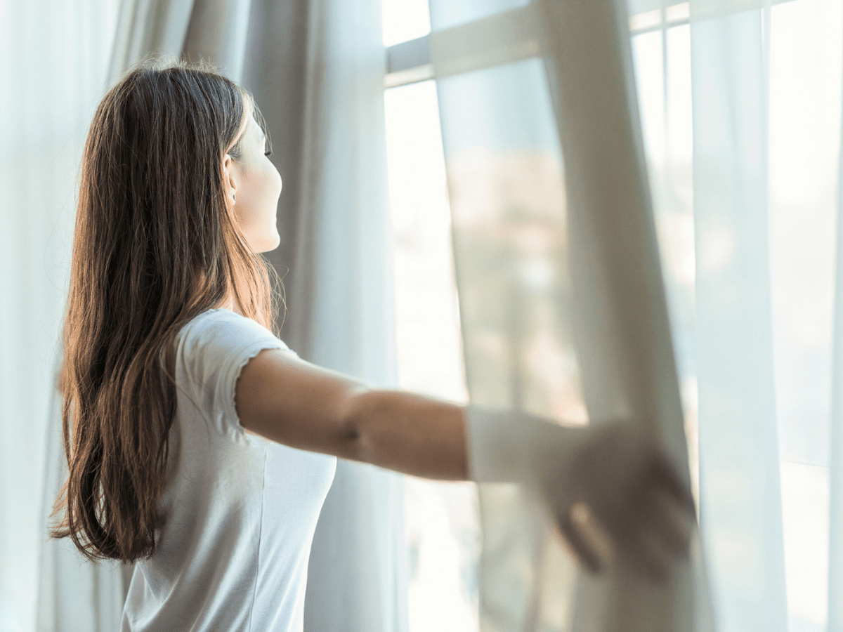 Frau steht am Fenster und schiebt Vorhänge zur Seite