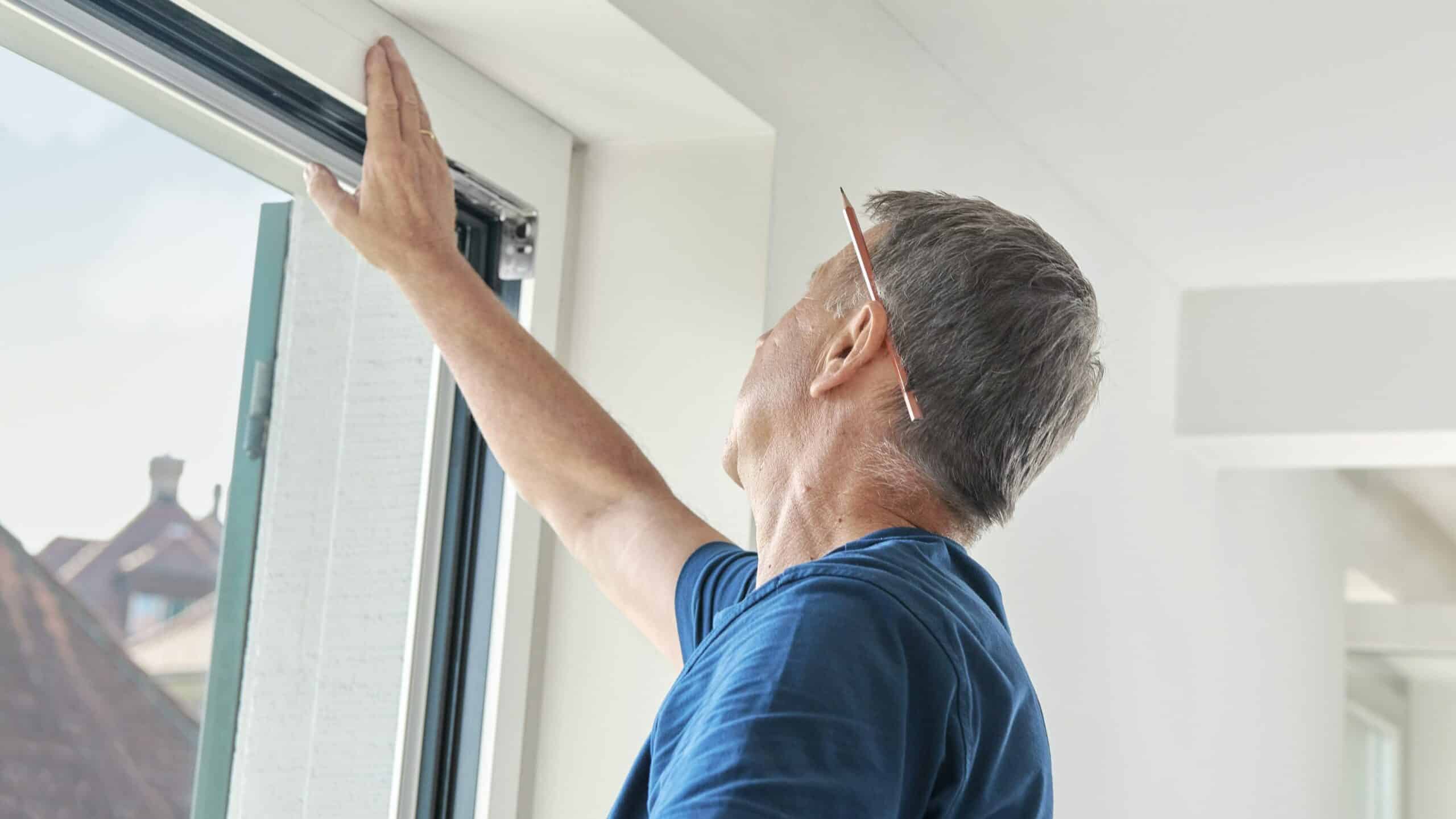 Monteur mit blauem T-Shirt prüft genaustens das Fenster