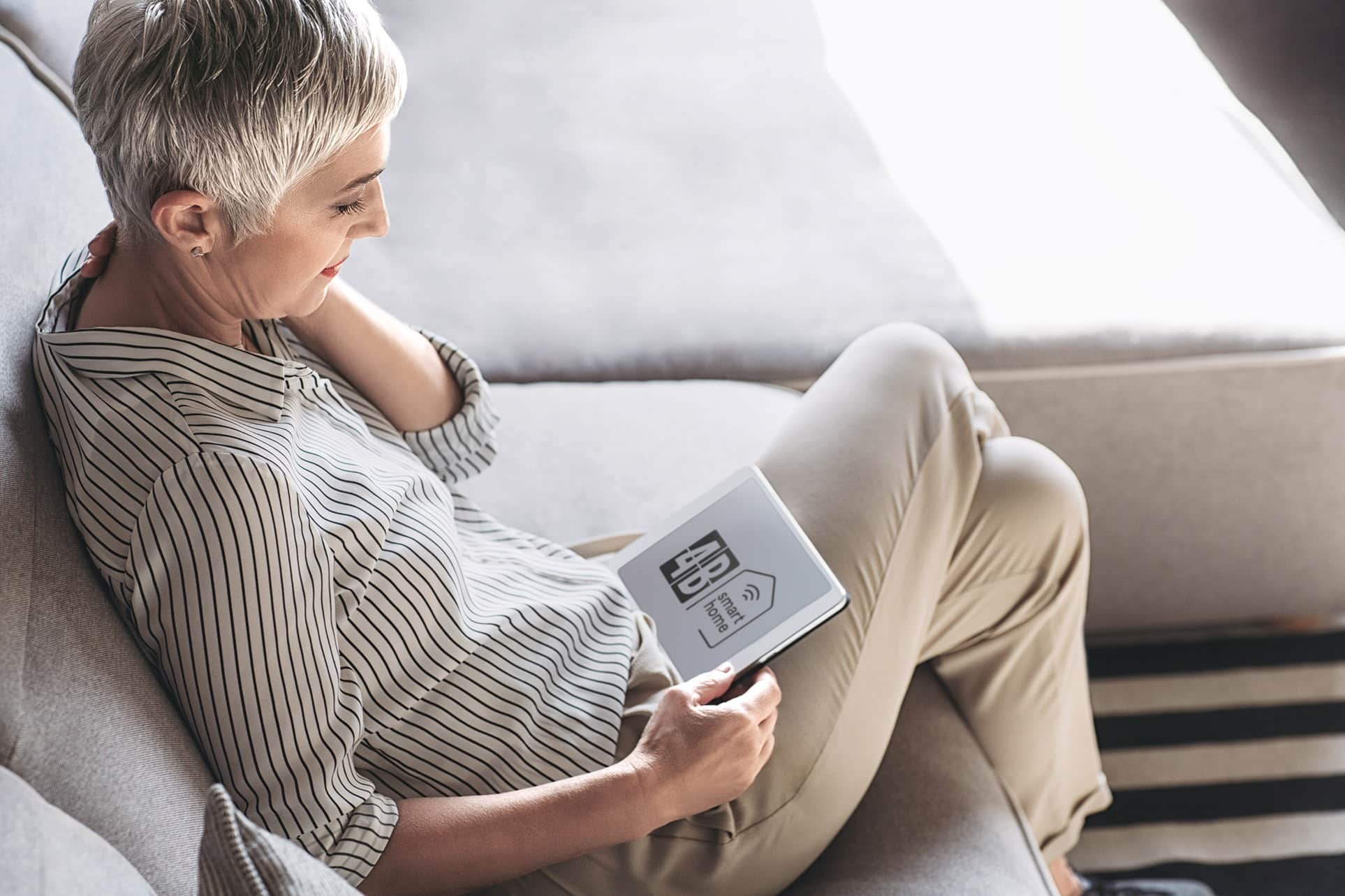 Einstiegsbild für die Medienseite - eine ältere Frau sitzt auf dem Sofa und liest auf ihrem Tablet.