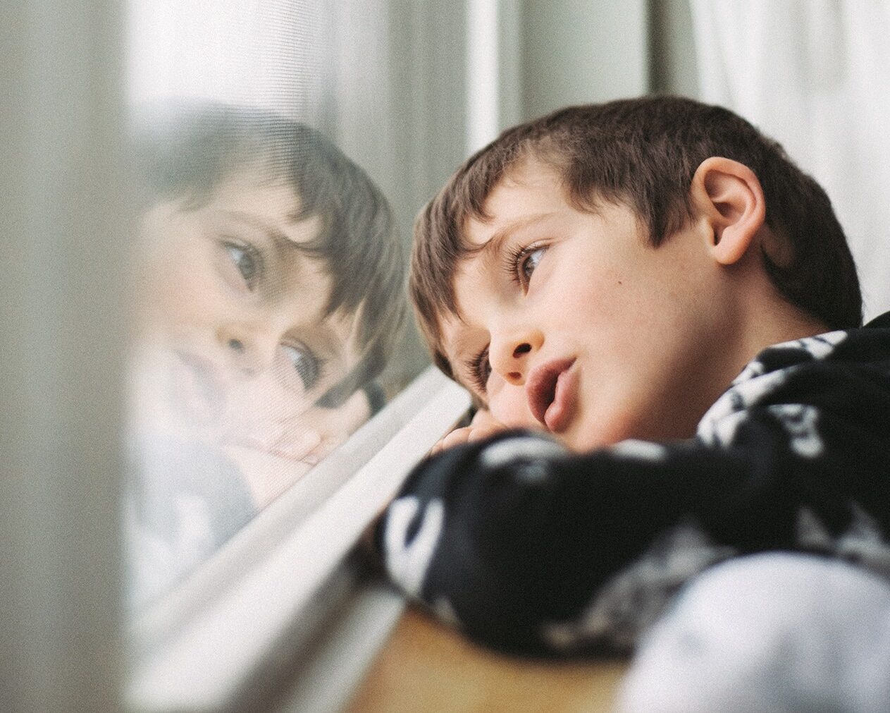 Kleiner Junge blickt verträumt aus Fenster