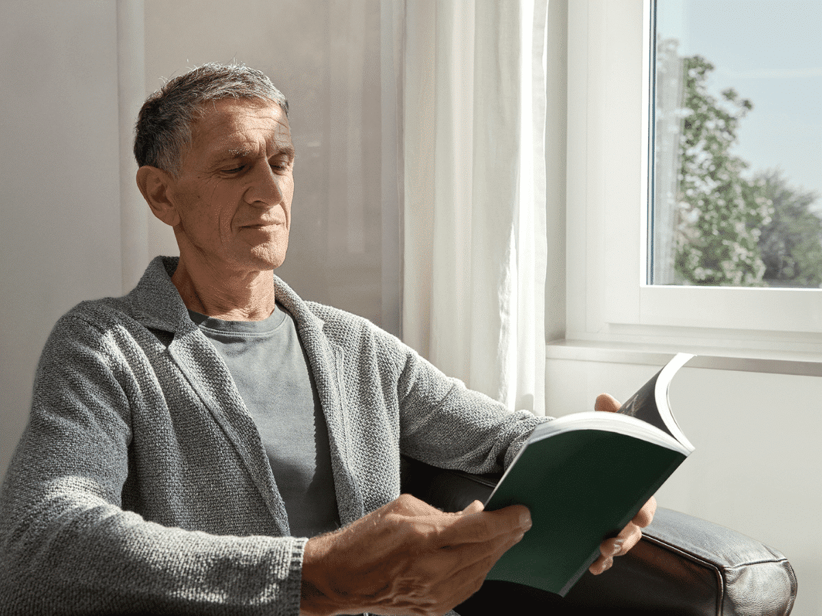 Mann liest entspannt ein Buch vor dem Fenster
