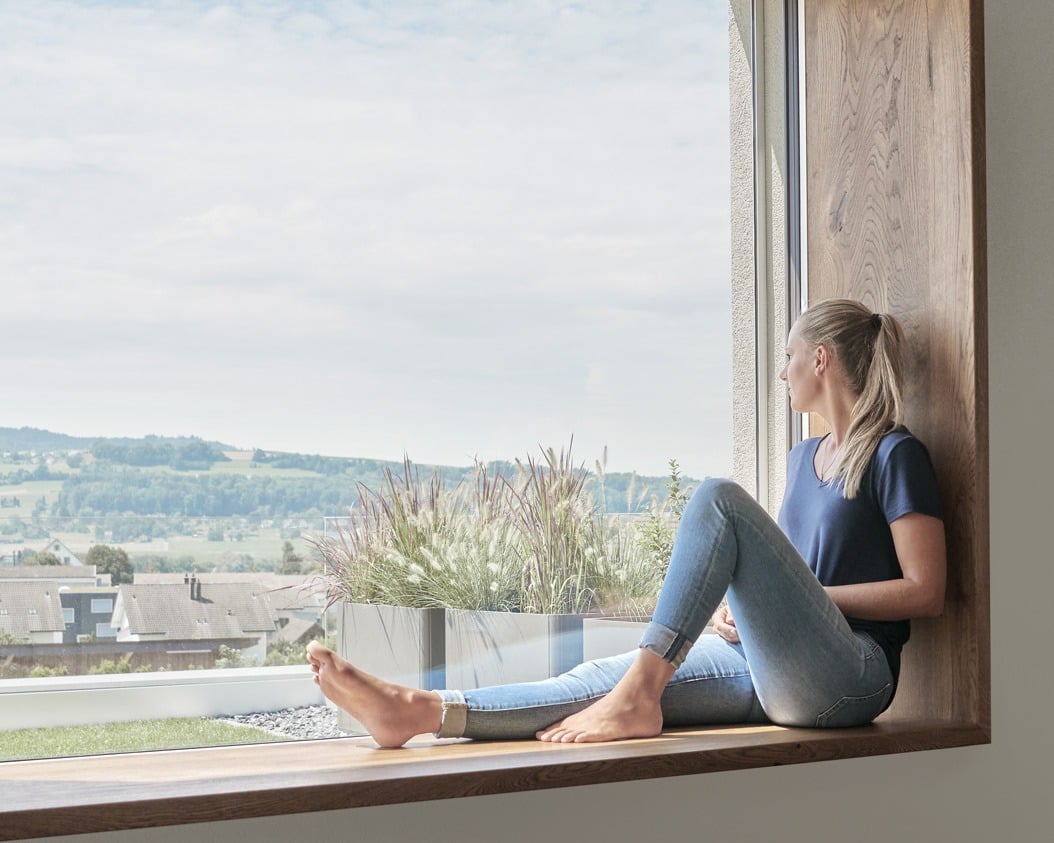Frau sitzt auf der Fensterbank und schaut aus dem Fenster