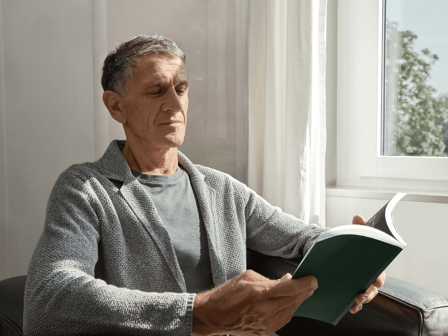 Älterer Mann liest entspannt ein Buch vor einem von der Sonne beschienen Fenster