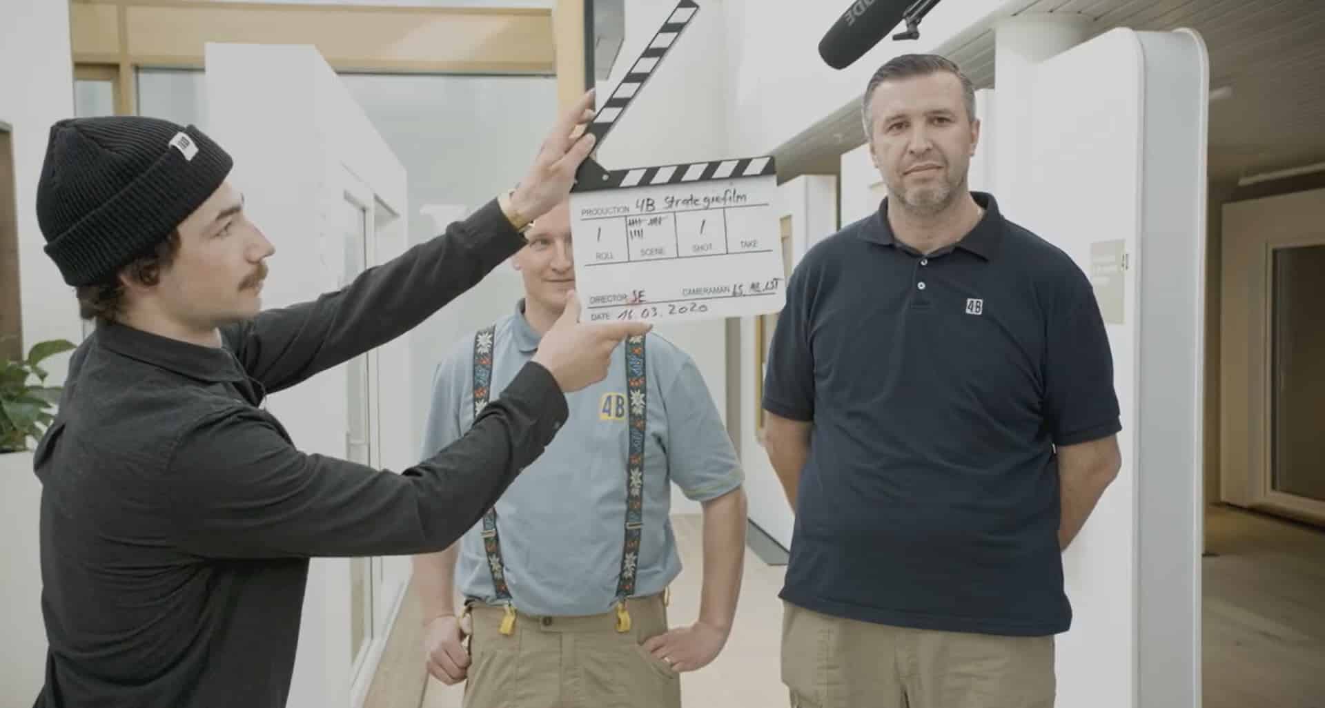 Mann mit Mütze hält Filmklappe vor zwei Produktionsmitarbeiter
