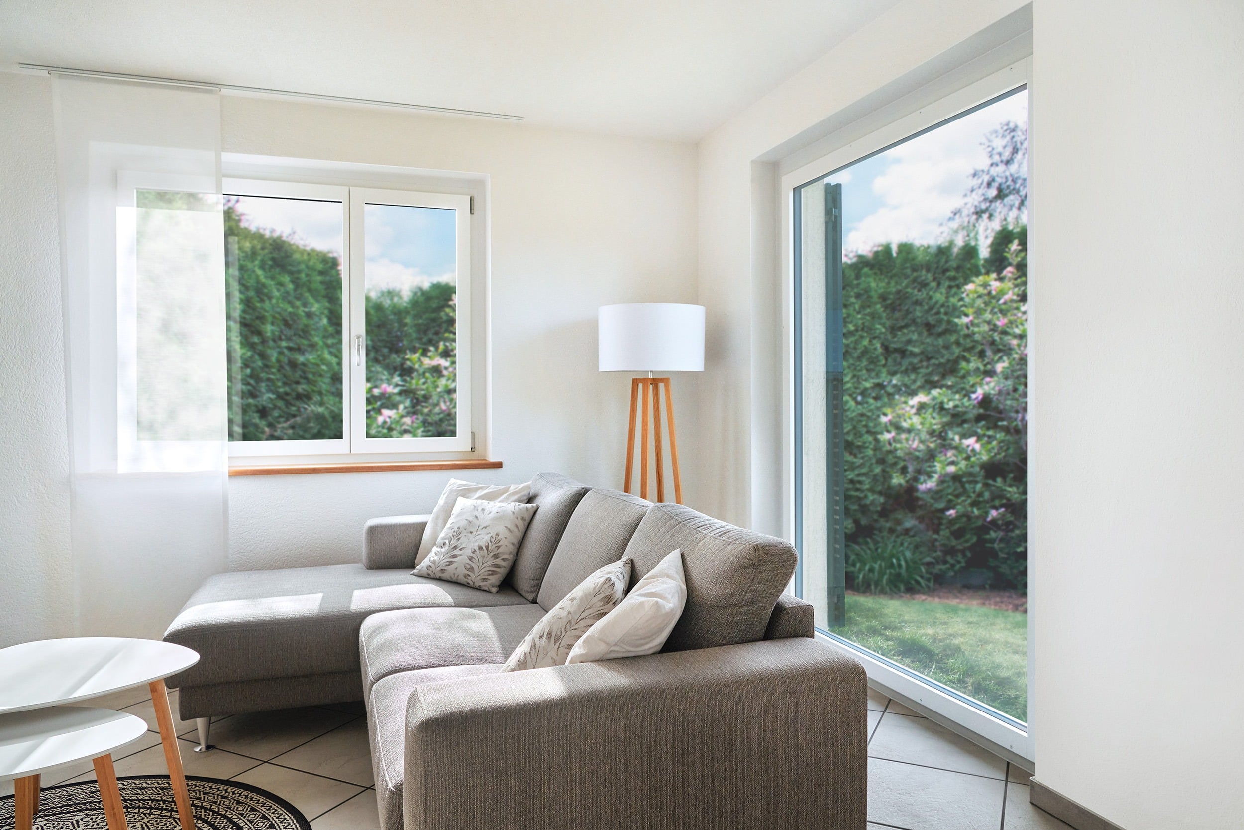 Wohnzimmer mit grauem Sofa, Kaffeetisch und grossen Fenstern.