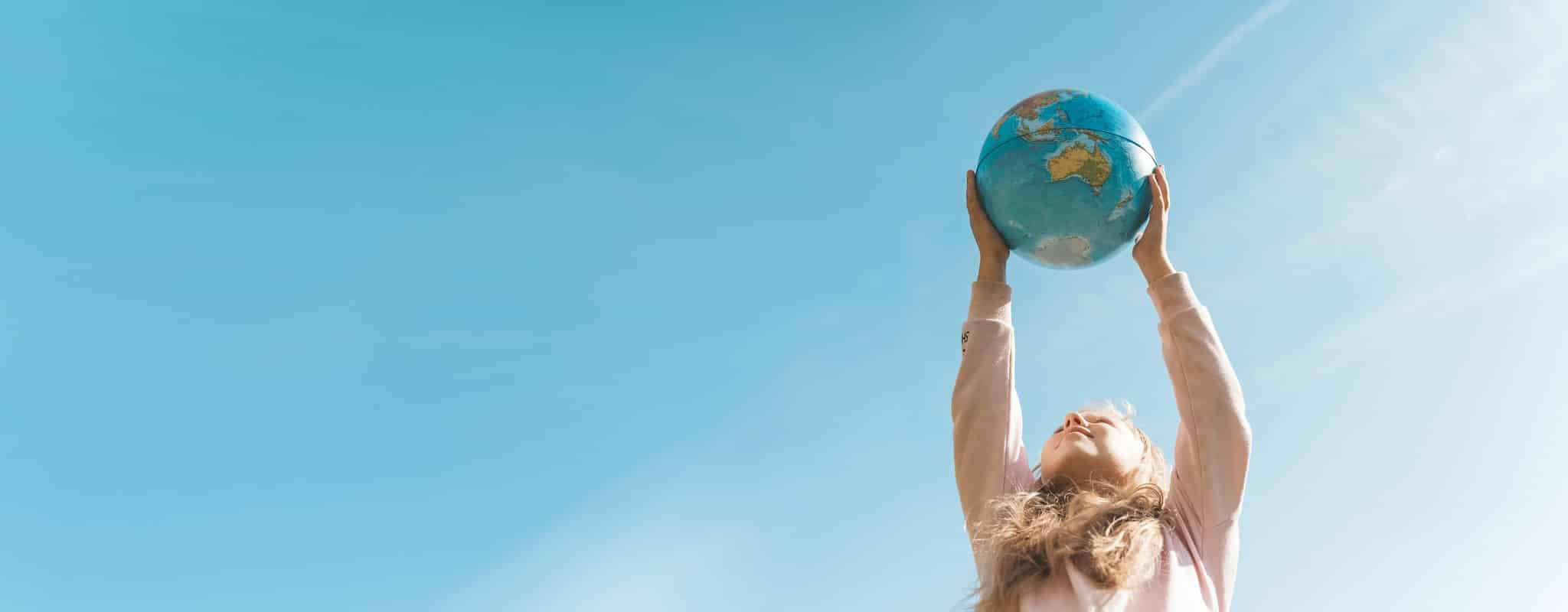 Energie sparen: Ein Mädchen hält eine Weltkugel mit beiden Händen und ausgestreckten Armen in die Höhe.